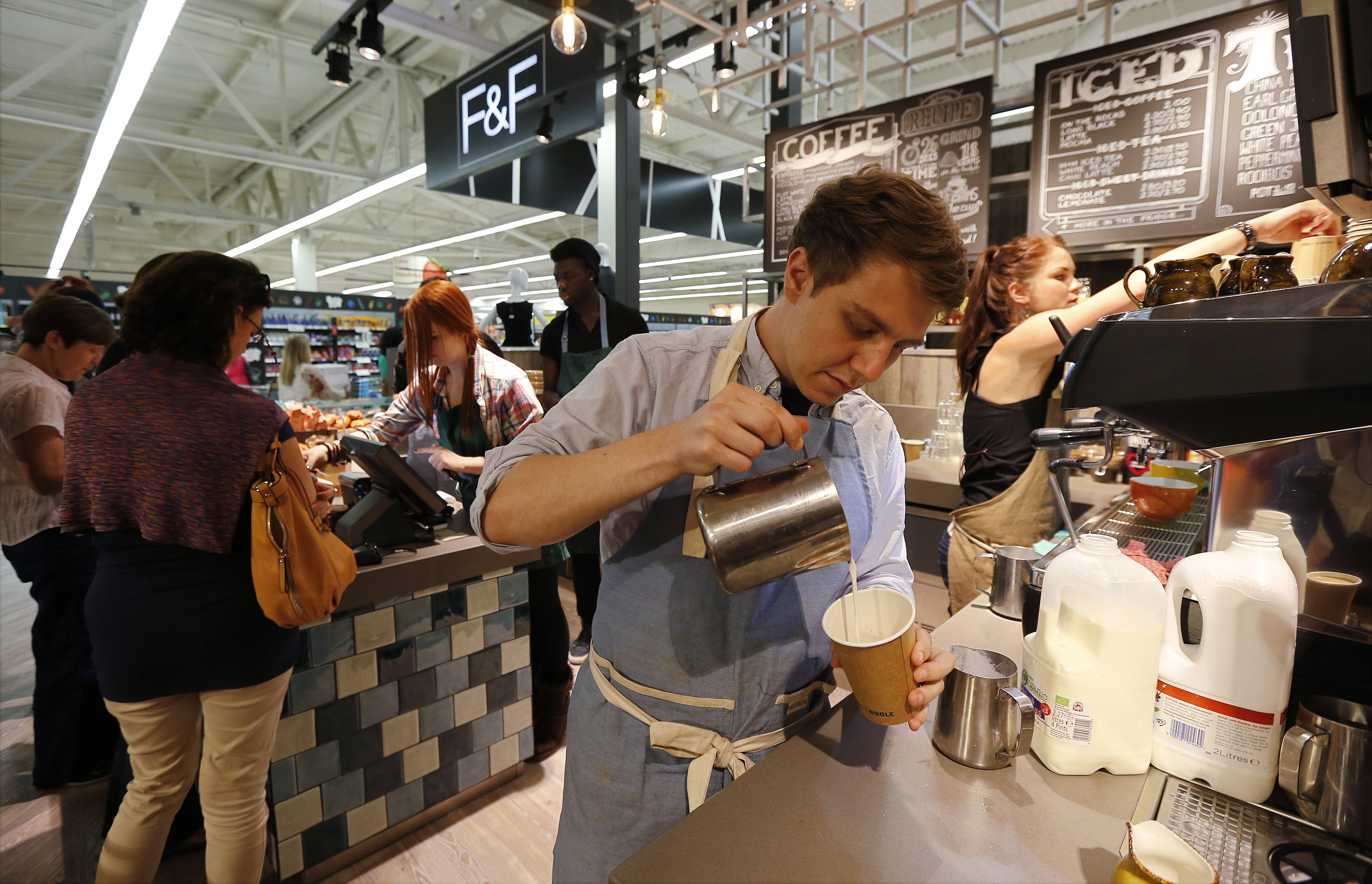 A barista makes a latte at the Harris and Hoole coffee shop inside a Tesco Extra supermarket in Watford, north of London August 8, 2013. Tesco, the world's number three retailer, is hoping the allure of casual dining, coffees and even yoga will help tempt Britons back to its ailing retail park stores as part of a 1 billion pound ($1.55 billion) push to revitalise business. REUTERS/Suzanne Plunkett (BRITAIN - Tags: BUSINESS FOOD) - RTX12DV0